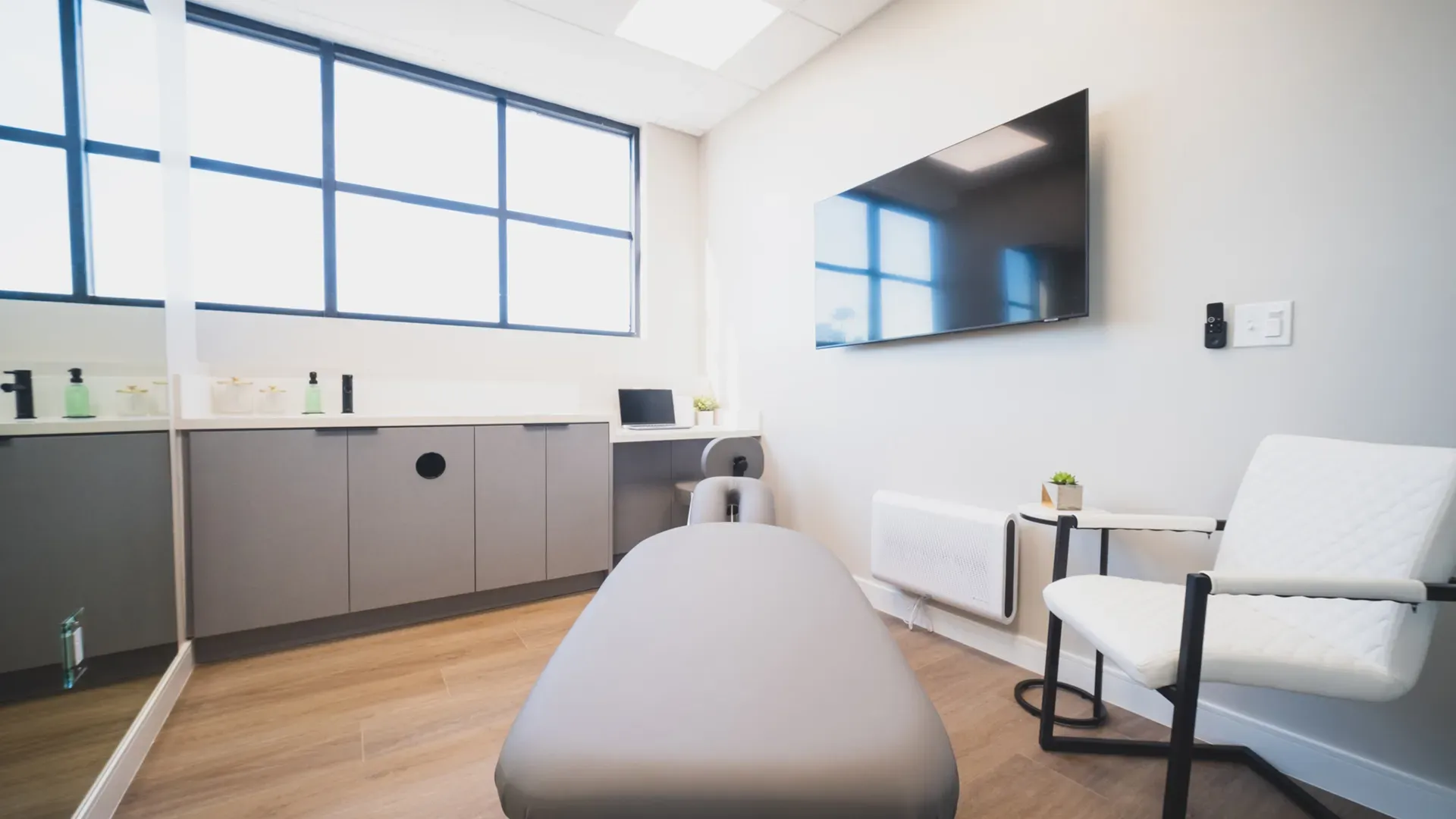 A treatment room with a padded table, a wall screen and a wide window