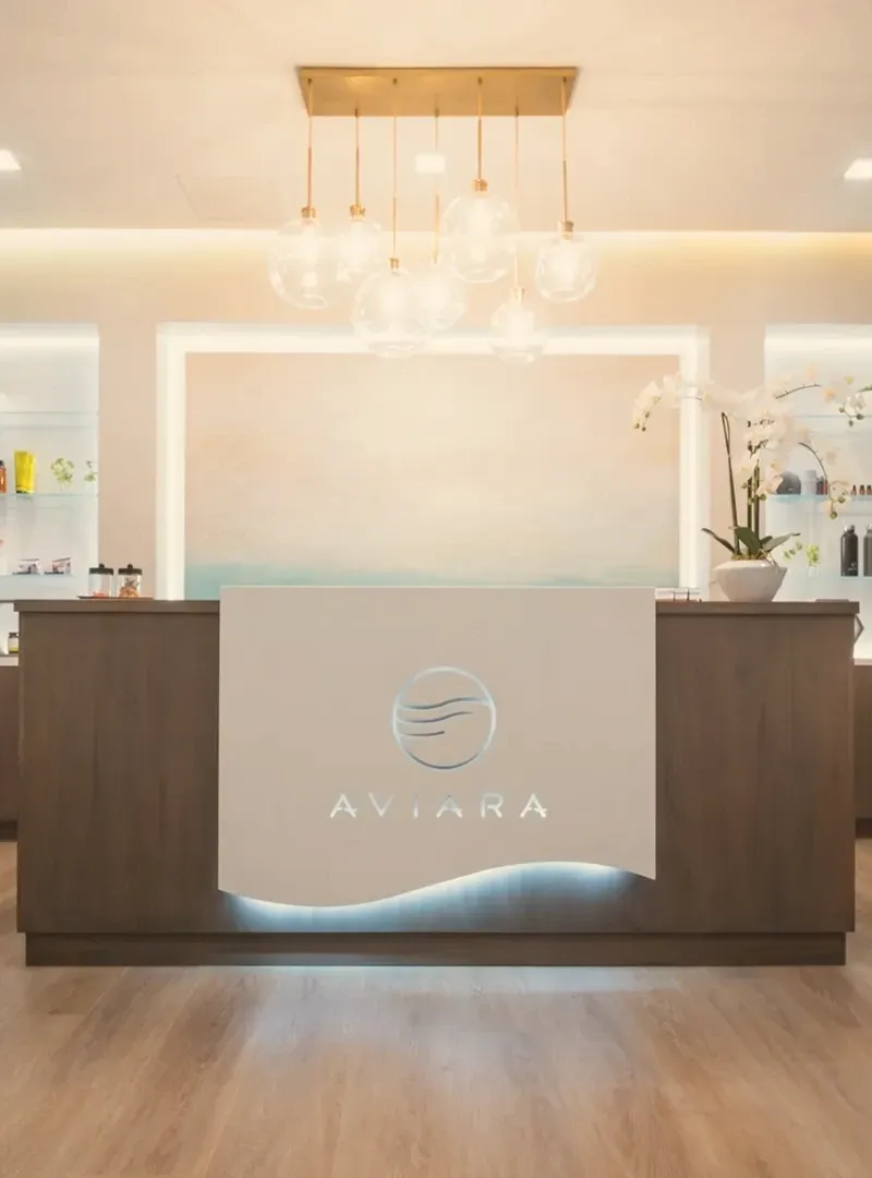 The reception desk at Aviara Centers, lit from below, with glass pendant lights and an orchid