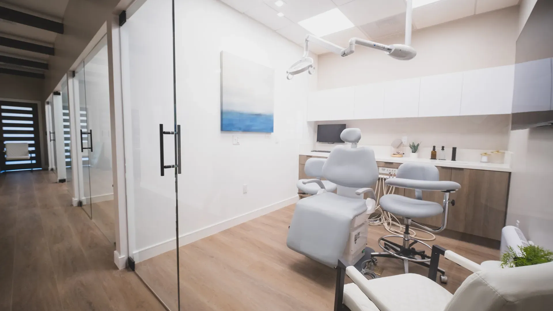 A glass-walled treatment room with a patient chair and consultation seating