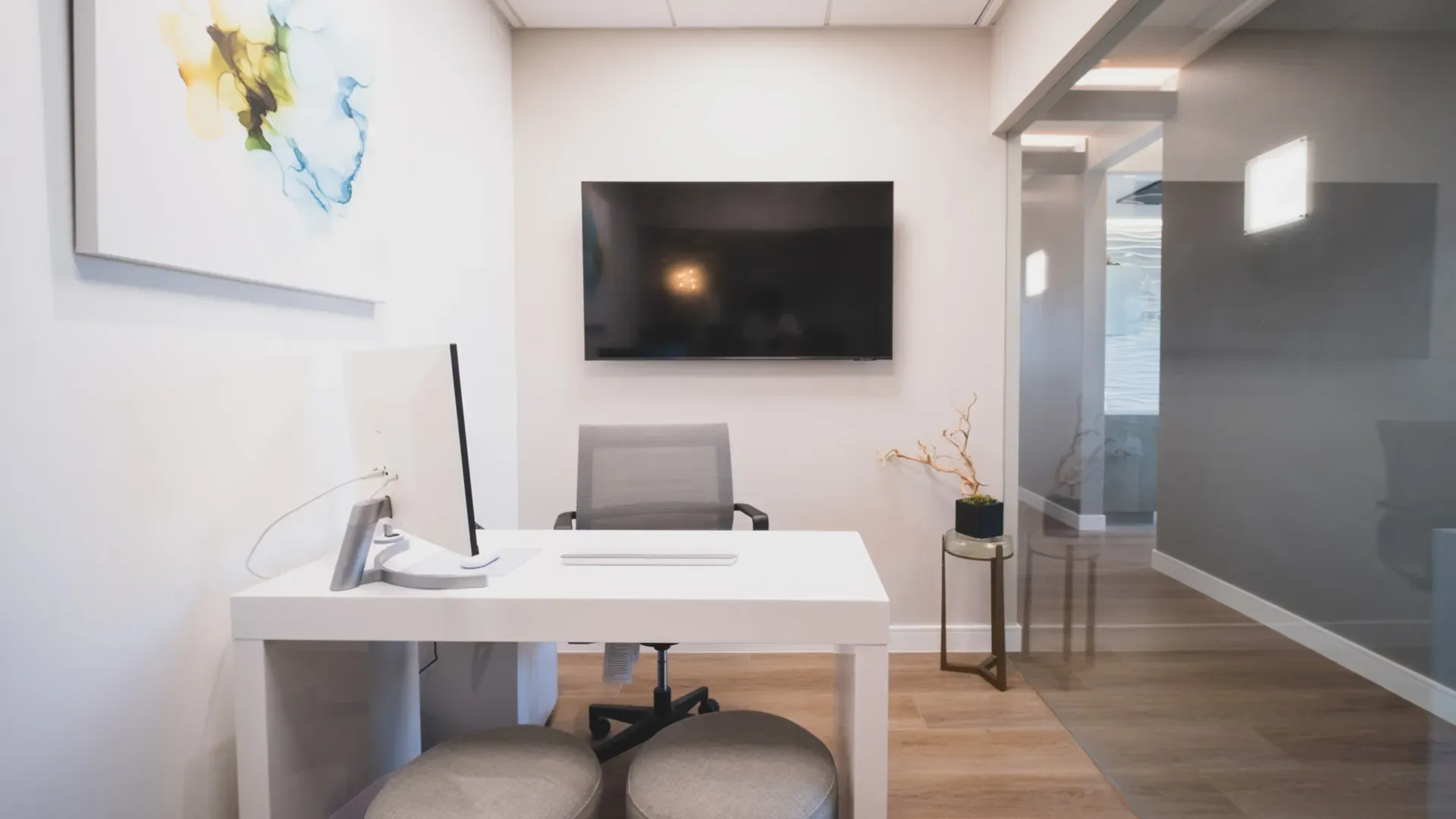 A consultation room with a white desk, a computer and a large wall screen